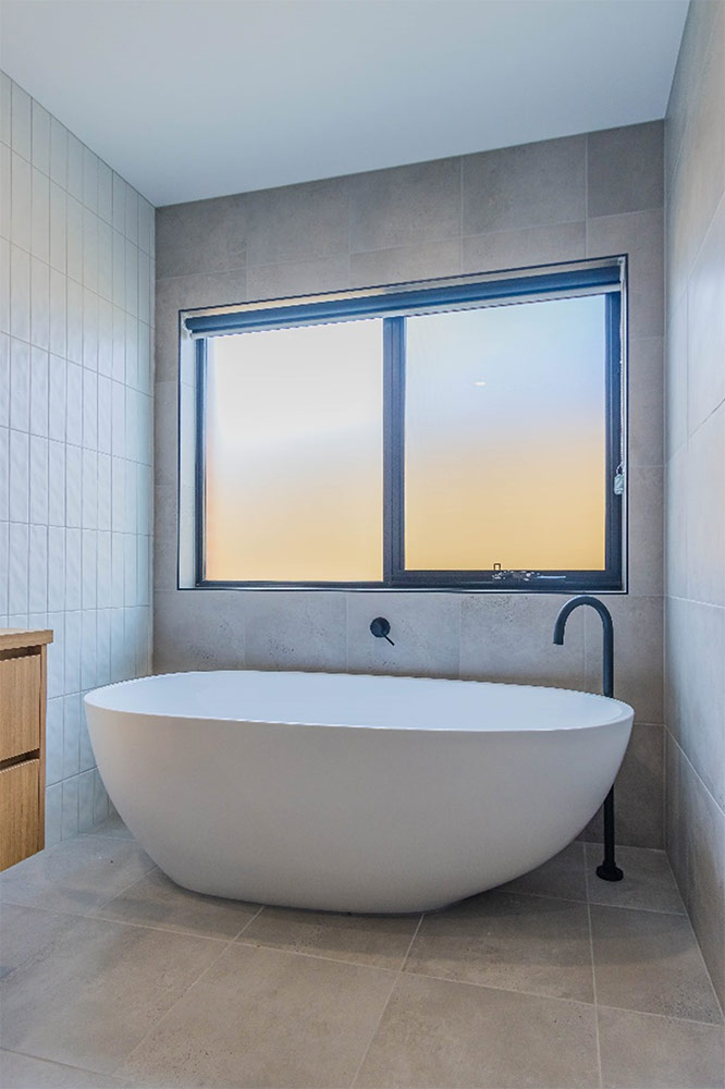 Photo of a modern white freestanding bathub in a bathroom, with a frosted window above the bath
