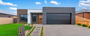 Contemporary facade of a home by Virtue Homes, with brown brick, white entrance, and charcoal grey garage.