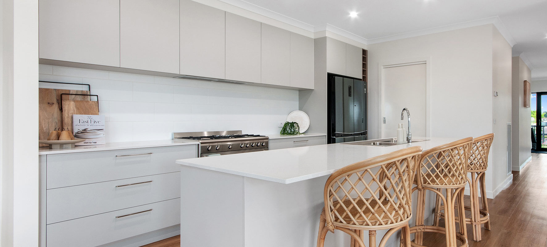 Photo of contemporary white and light grey kitchen, black fridge and cane stools at the island bench