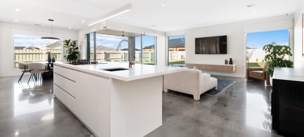 Living area of display home with white kitchen island bench and white couch.