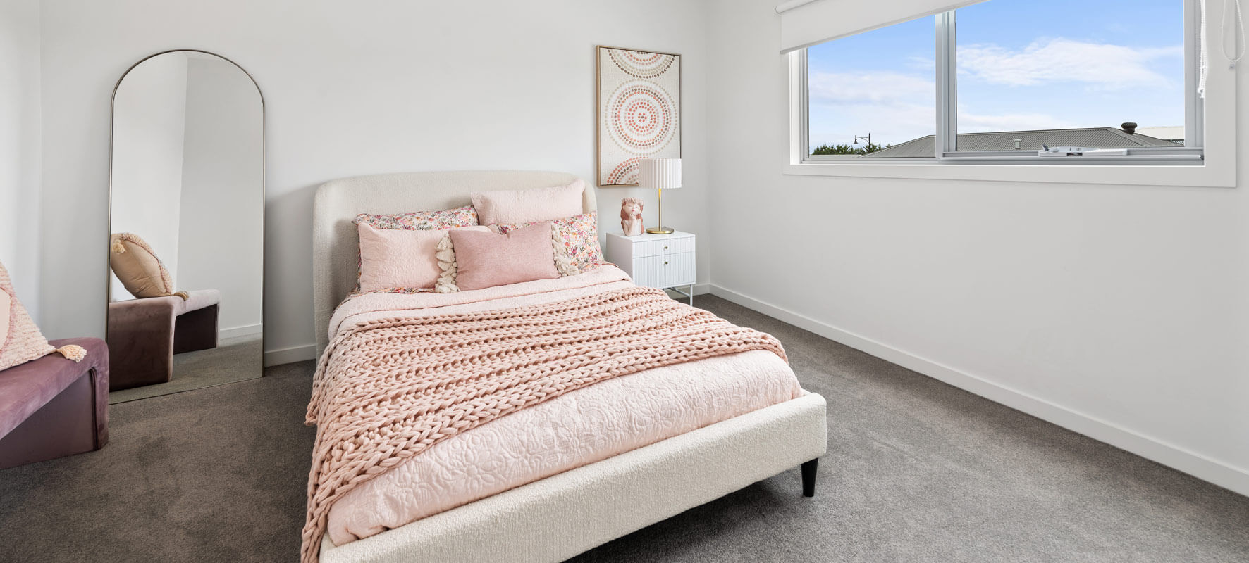 Photo of peaceful looking bedroom with white bed and soft pink cushions and blankets