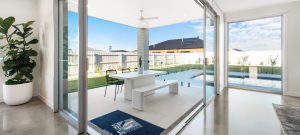 Photo of outdoor living area wiht white table and chairs and grass backyard and inground pool in the background