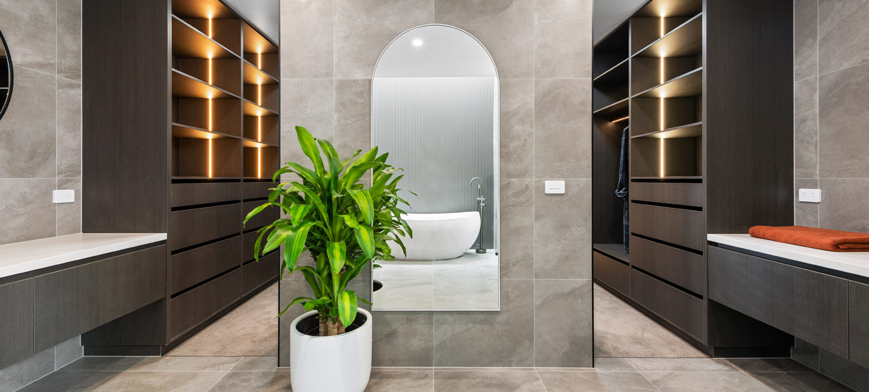 Photo of luxury bathroom ensuite with grey tiles, large full length mirror with rounded top and in the background dark timber wardrobe cabinetry
