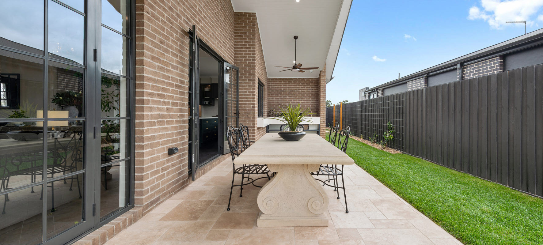 Photo of outdoor living area in Ranch style home showing stone table with black wrought iron chairs.