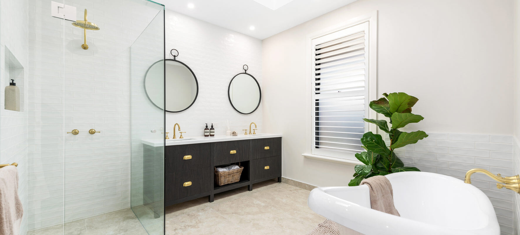 Photo of bathroom in Ranch style home showing white bathtub, timber vanity with two sinks and clear glass shower