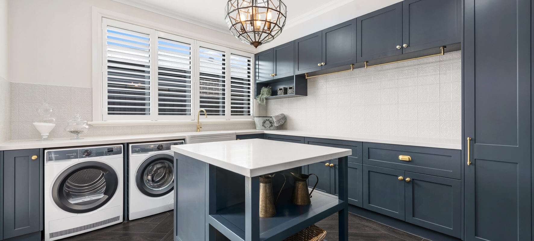 Photo of large laundry in Ranch style home showing navy blue cabinets, centre island cabinets with white stone benchtops.