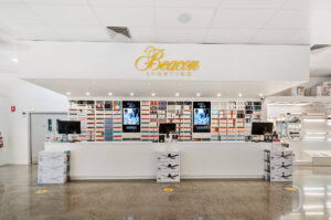Photo of the front counter at Beacon Lighting store, with long white counter, yellow sign above the counter, and rows of gloves and lights behind and surrounding the counter.