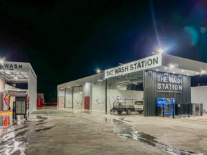Photo of a modern new car wash business at night with driveway, auto car wash and bays for people to wash their own cars.