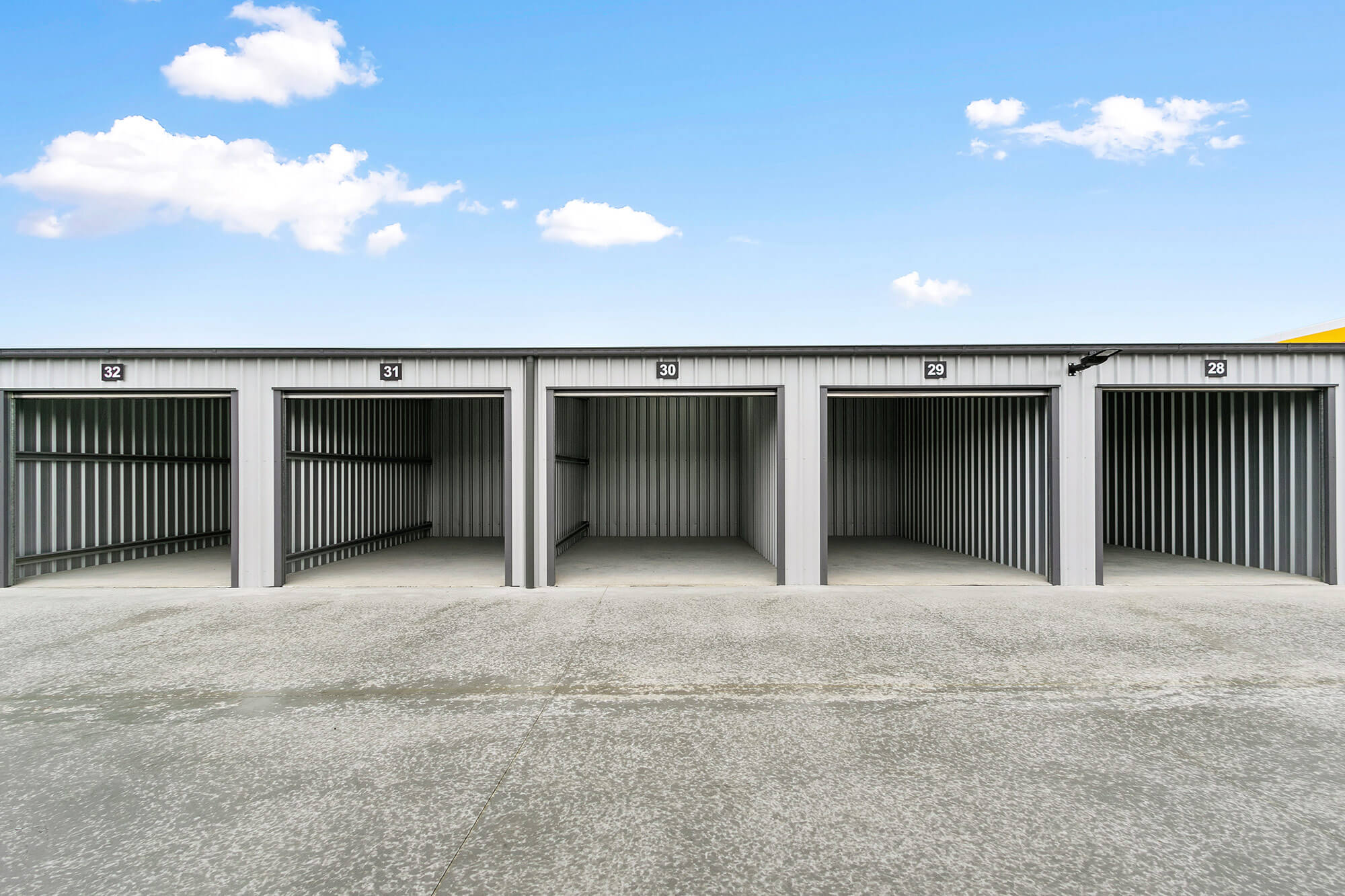 Photo of new storage shed facility, with rows of grey storage shed with black roller doors. Doors are open.