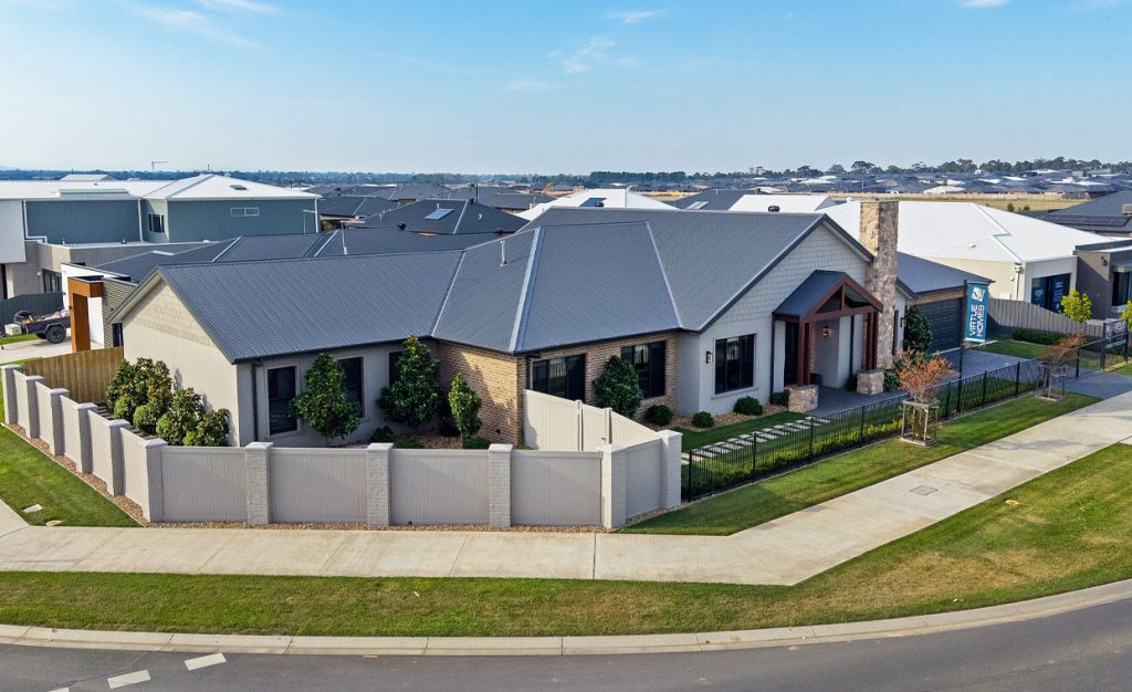 Facade of Ranch style Display Home with stone, timber and brick exterior in warm tones, and charocal colour tin roof. The home is a sprawling, luxury ranch style home set on corner block.