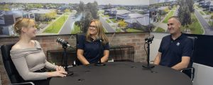 Two women and a man sitting at a table recording a podcast for Virtue Homes about the process of building a custom home.