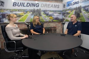 Two women and a man sitting at a table recording a podcast for Virtue Homes about the process of building a custom home.