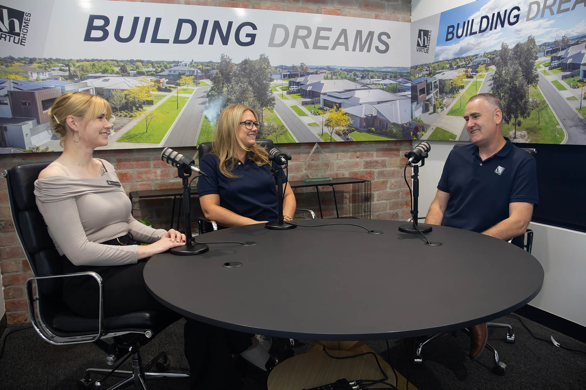 Two women and a man sitting at a table recording a podcast for Virtue Homes about the process of building a custom home.