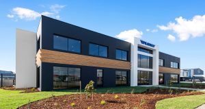 Facade of a large two storey commercial building with charcoal render, white entry and timber stripes between the two levels.