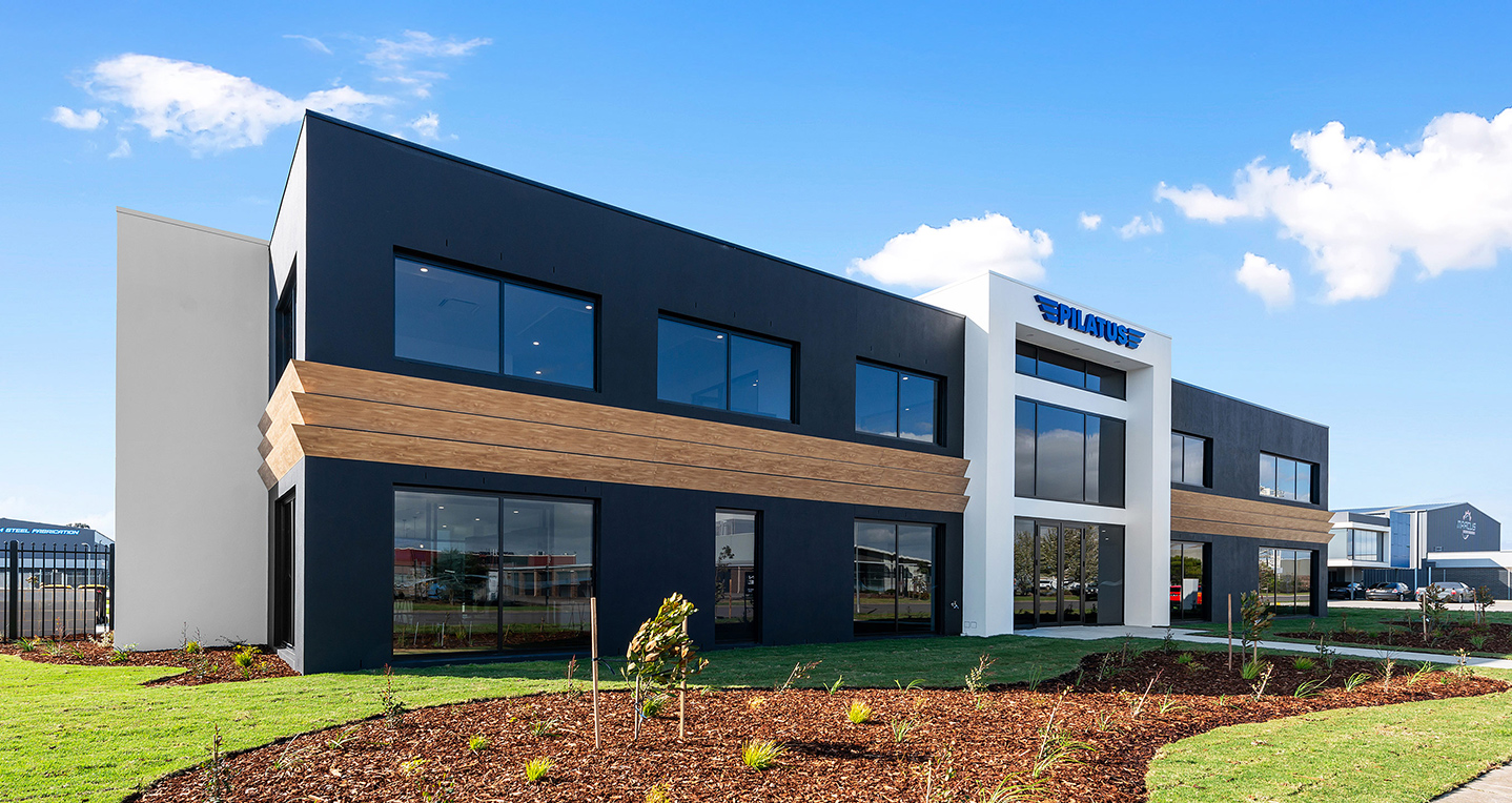Facade of a large two storey commercial building with charcoal render, white entry and timber stripes between the two levels.