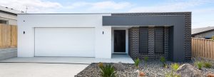 Facade of a flat roof, modern style contemporary new home with white rendered garage and dark brick house.