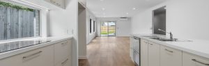 White gallery style kitchen and empty living room with timber look vinyl flooring